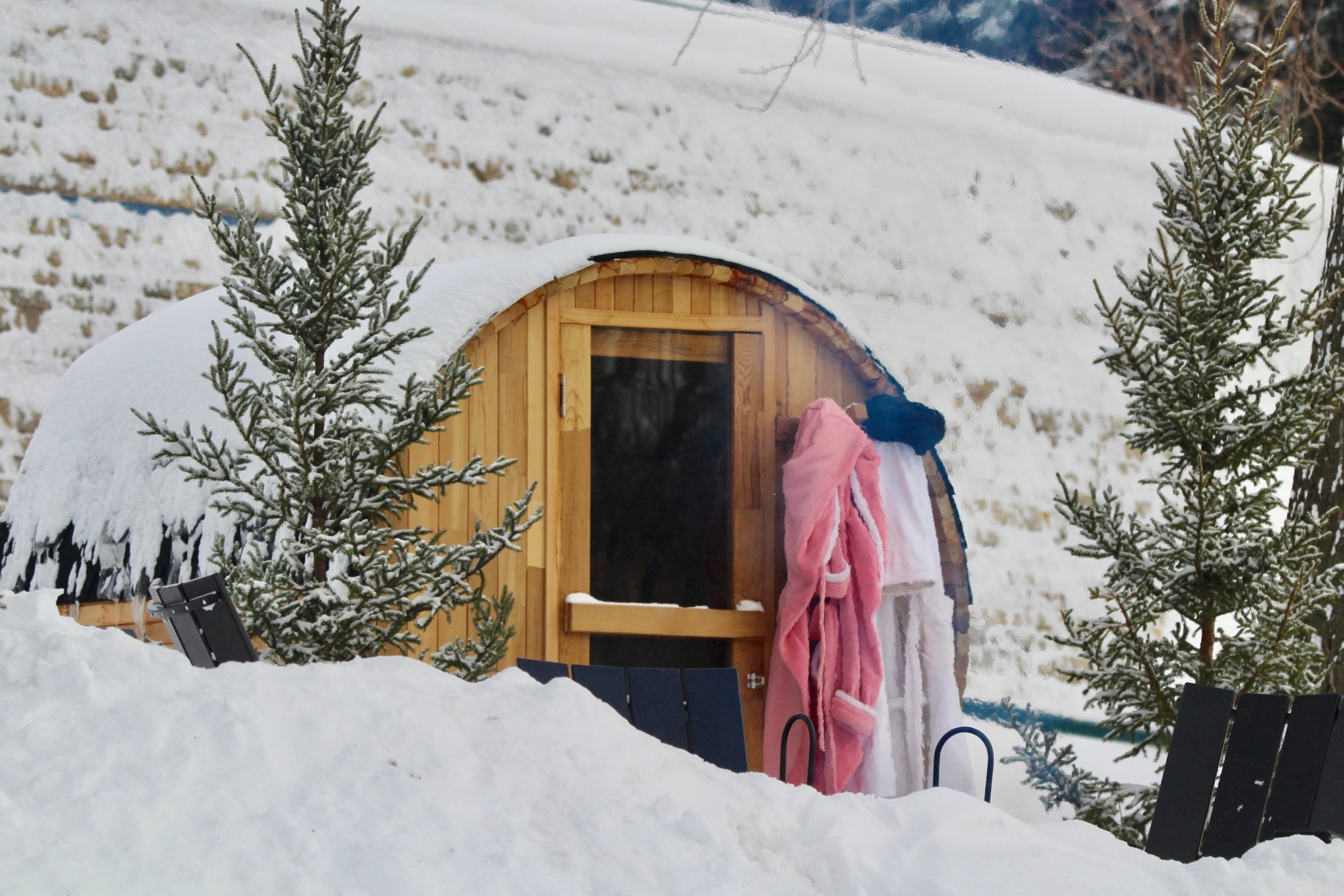 Snow covered barrel sauna with bathrobes.