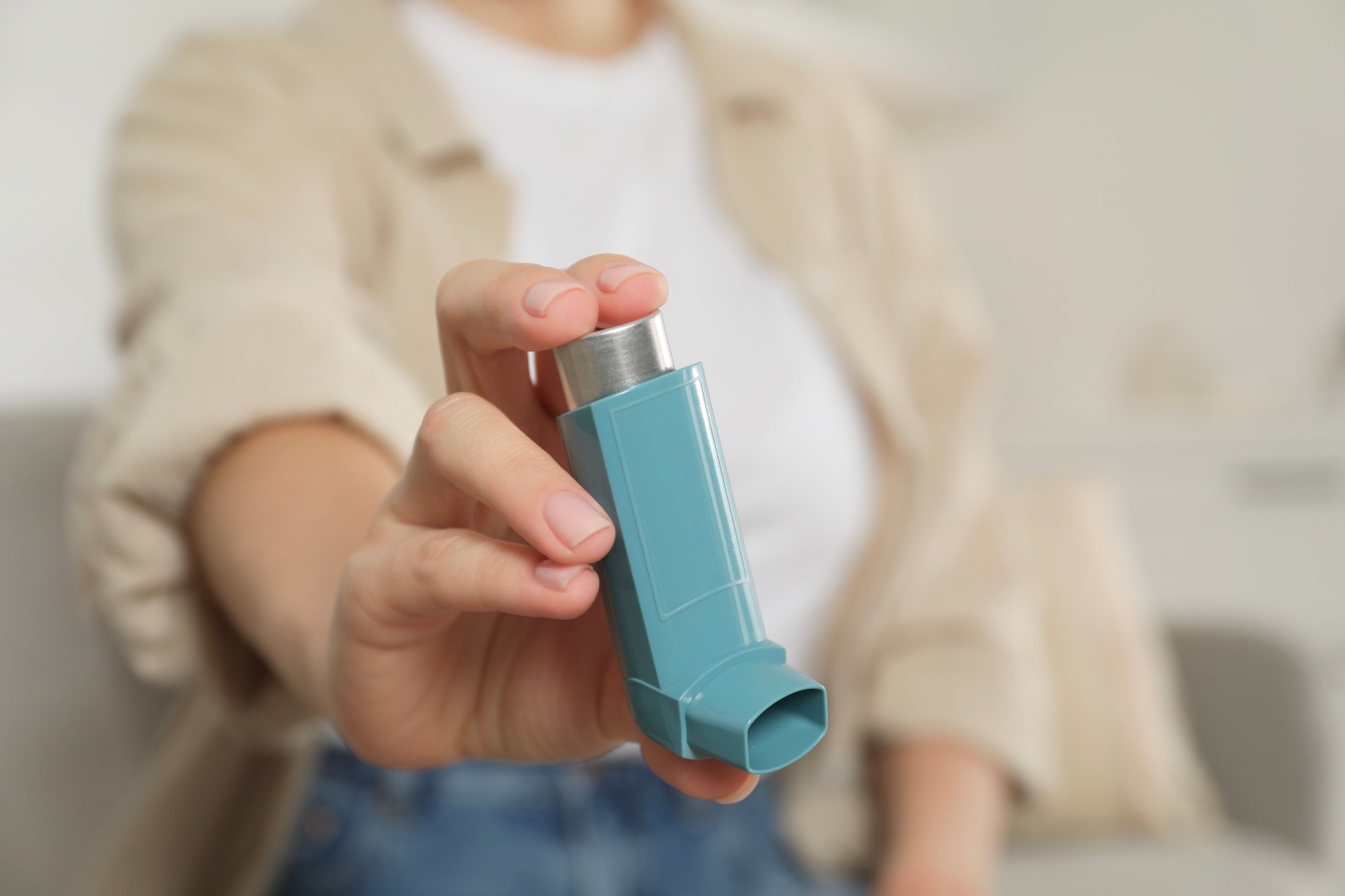 Woman holding asthma inhaler indoors, closeup