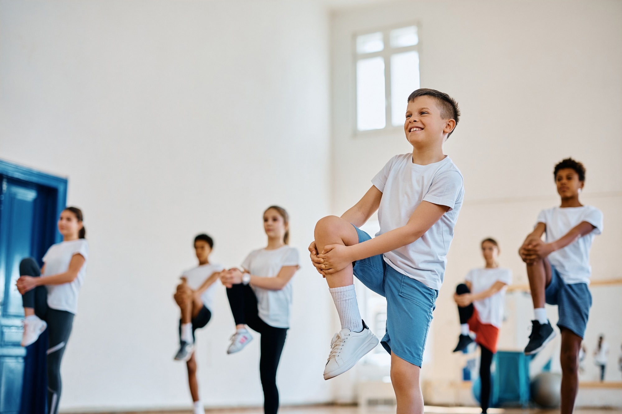 Happy student and his classmates practicing on PE class at school gym.