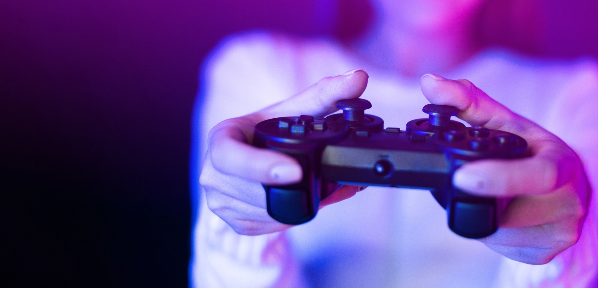 A woman is seen holding a video game controller in front of a vibrant purple light, engaged in a gaming session.