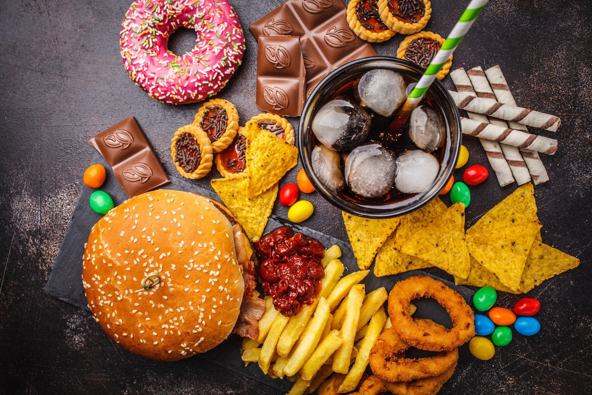 Burger, sweets, chips, chocolate, donuts, soda on a dark background.