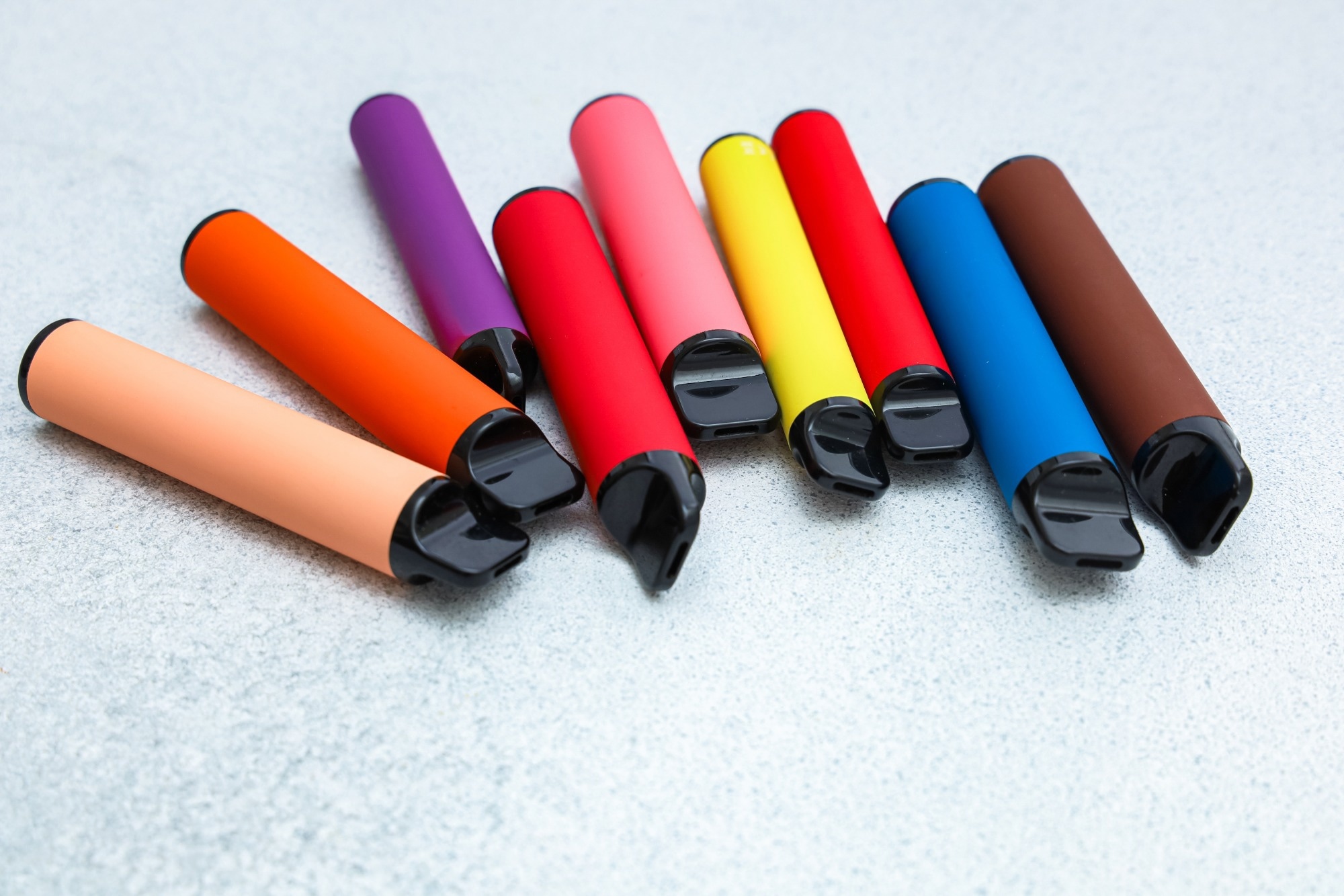 Collection of colorful vape pens arranged on a neutral gray surface.