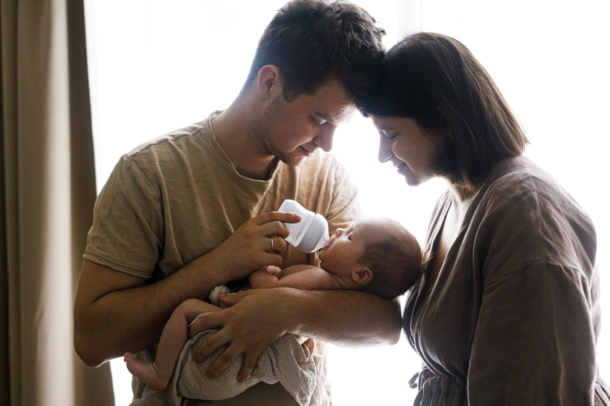 mother and father feeding little baby son with bottle