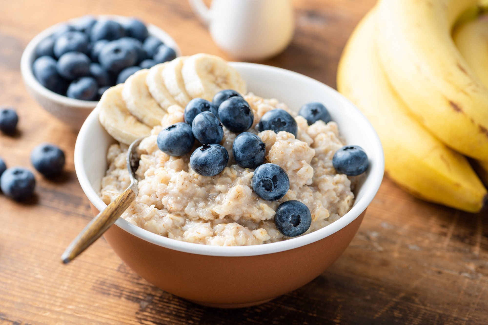 oatmeal porridge with fresh blueberries and banana slices in bowl on wooden table background, closeup view