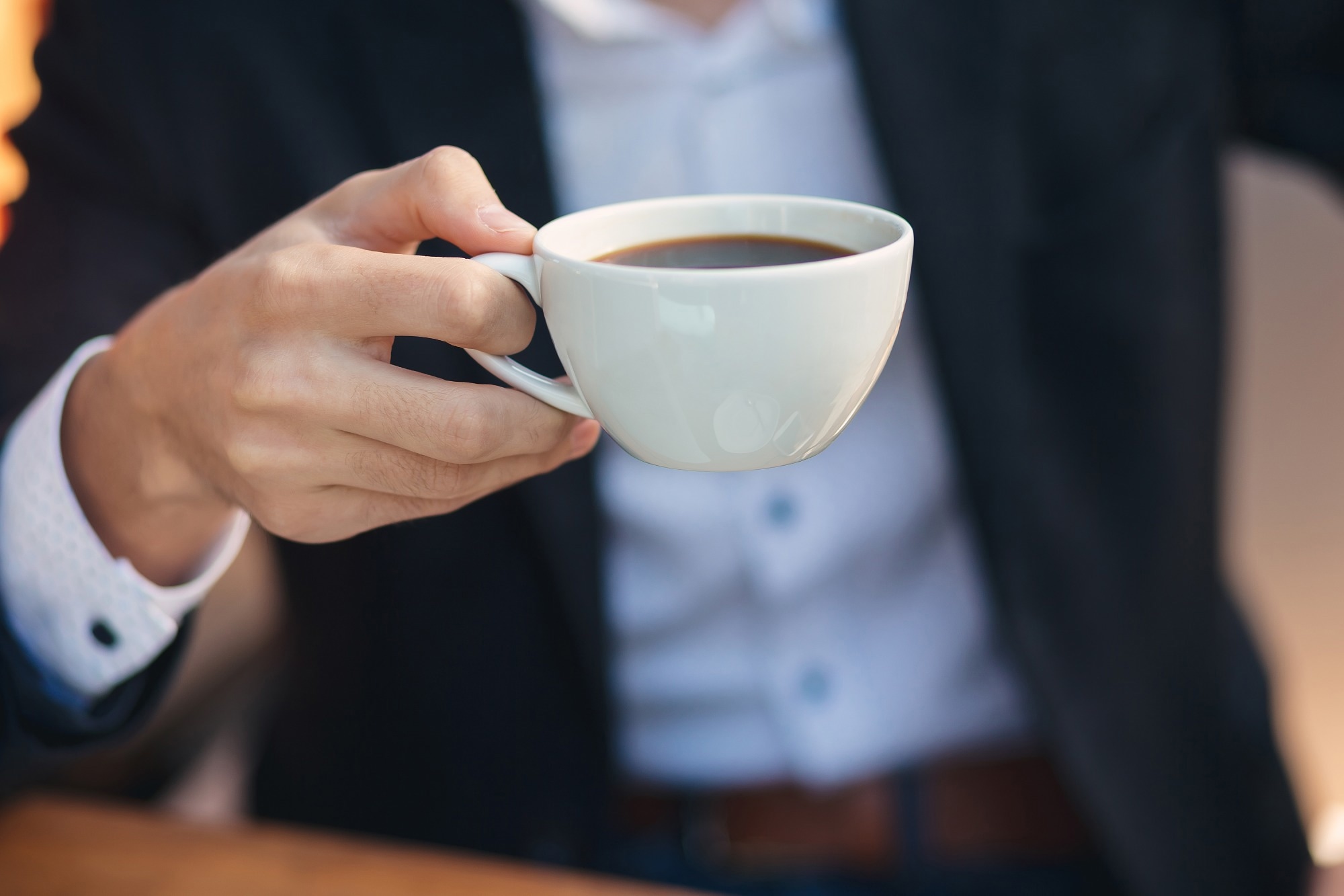 Close-up hand of young businessman in formal wear holding cup, mug of coffee
